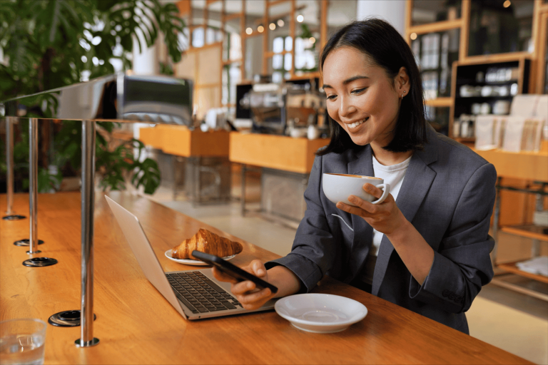 Mujer sonriente en cafetería usando su celular mientras toma café