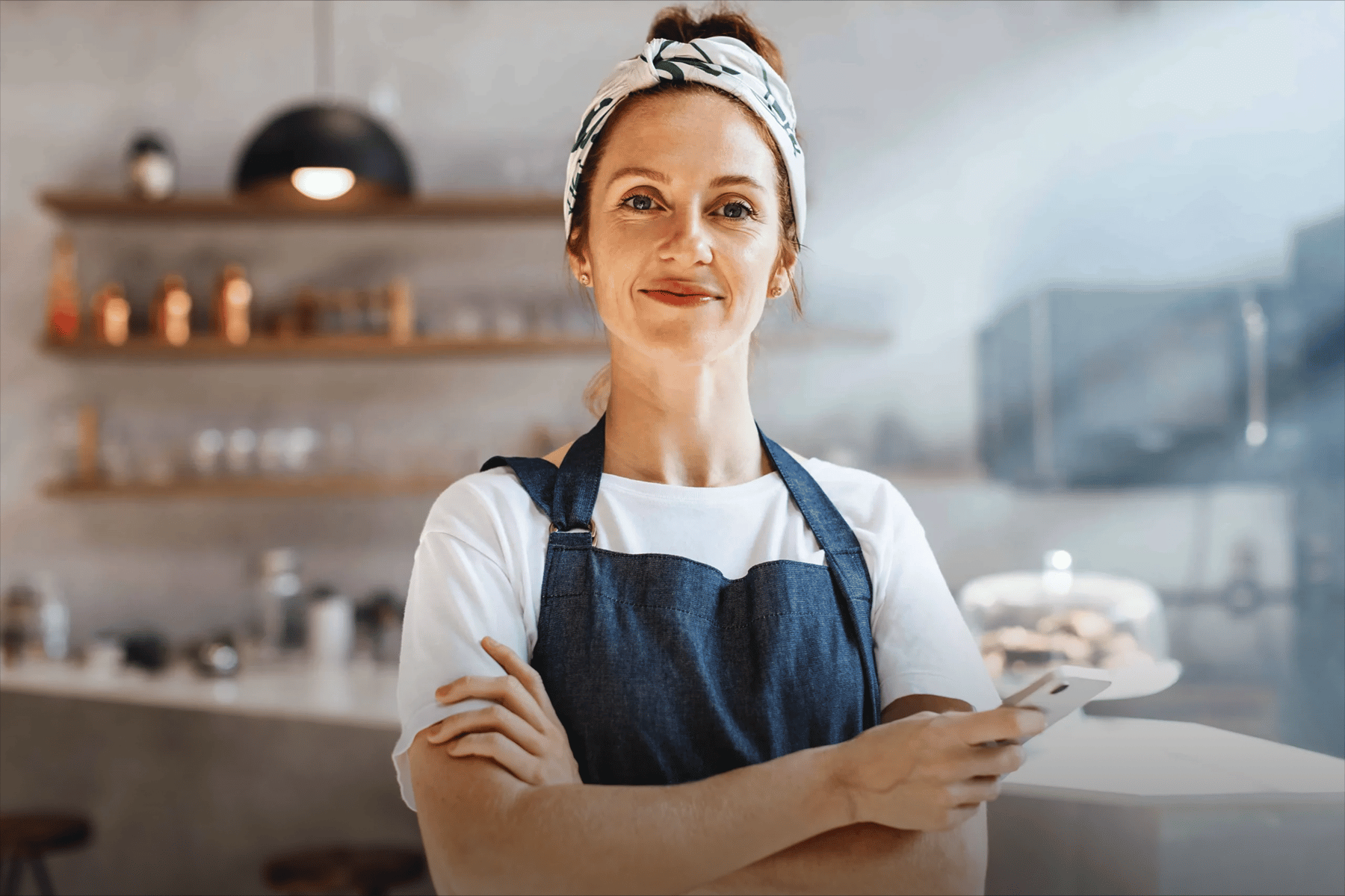 Mujer emprendedora con delantal sosteniendo un celular en su cafetería