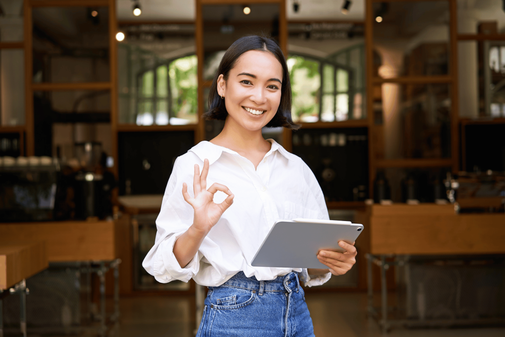Emprendedora sonriendo con tableta y señal de OK en cafetería