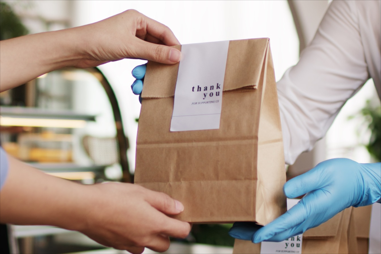 Cliente recibiendo pedido para llevar en bolsa de papel con etiqueta de agradecimiento